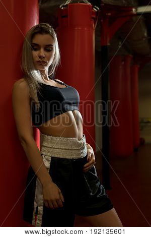 Sexy girl in top and miniskirt posing by punching bag in a gym