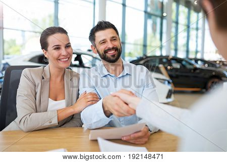 Young couple with car dealer in auto salon