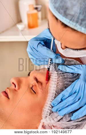 Filler injection for male face. Plastic facial surgery in beauty clinic. Man anti-aging therapy for complexion. Doctor in medical gloves with syringe forehead injects . Watches appearance concept.