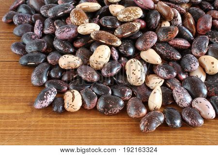 Raw purple, pink, beige with brown speckled kidney beans on brown wooden table. Closeup
