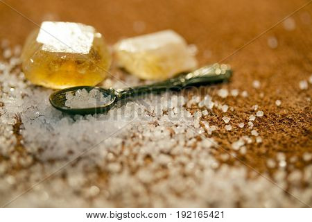 Tiny spoon filled with sweet sugar crystals at a light brown background