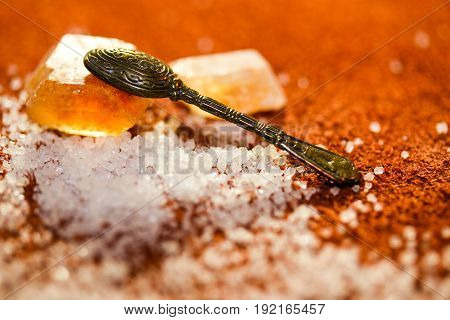 Tea spoon on the sweet crystal of sugar at a light brown background