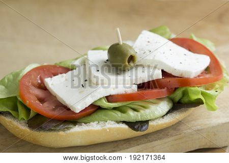 open baguette whit Mexican Panela cheese, tomato, lettuce, salt, pepper and olives at the top