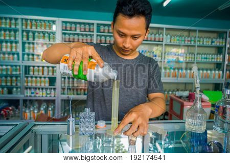 BALI, INDONESIA - MARCH 08, 2017: Unidentified man using syringes and pipettes mixing essences to prepare perfumes for the perfume store in Denpasar Indonesia.