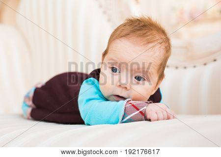 Adorable baby boy with red hair and blue eyes. Newborn child lyling in couch