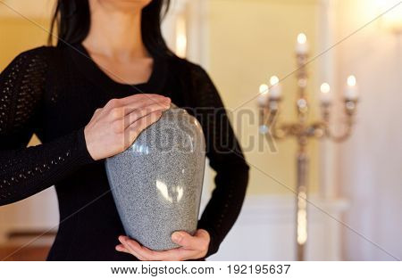 cremation, people and mourning concept - close up of woman with cinerary urn at funeral in church