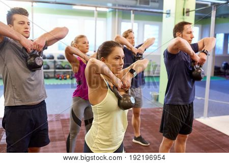 sport, fitness, weightlifting and training concept - group of people with kettlebells and heart-rate trackers exercising in gym