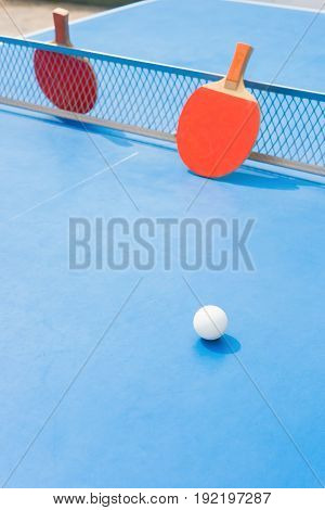 pingpong rackets and ball and net on a blue pingpong table