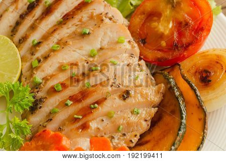 Sliced chicken breast barbecue on white plate served with grilled vegetable. Delicious chicken breast steak and salad for dinner. Homemade chicken breast barbecue on wood table for background. Chicken barbecue or pork steak close up view.