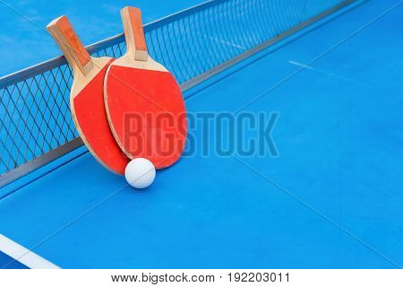 pingpong rackets and ball and net on a blue pingpong table