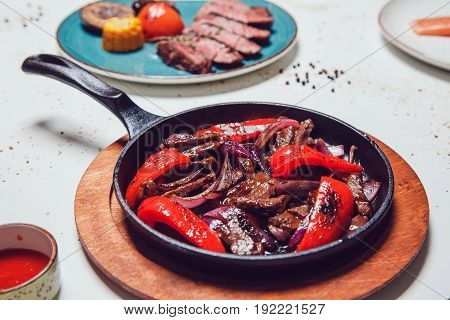 Mexican fajitos in a frying pan on a white table.