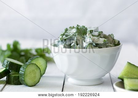 Cucumber salad with coriander and yogurt dressing on the white wooden background