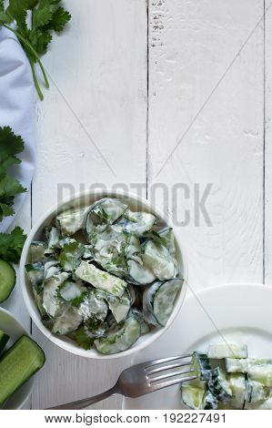 Cucumber salad with coriander and yogurt dressing on the white wooden background