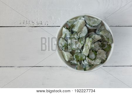 Cucumber salad with coriander and yogurt dressing on the white wooden background