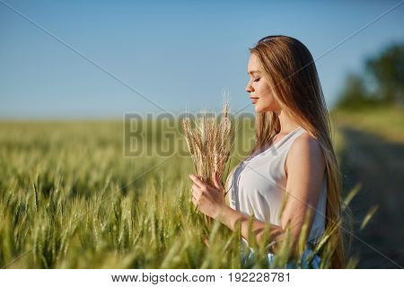 Beautiful happy woman girl smiling outdoors on green wheat field in summer nature. Pretty woman with natural makeup curly hairstyle in country village with green wheat. Attractive beauty girl in park