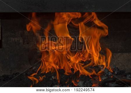Orange flames blaze and dance brightly inside the coal forge