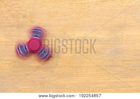 Red fidget spinner in motion stress relieving toy on a yellow wooden background