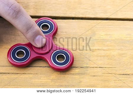 Caucasian man holds his finger (hand) Red fidget spinner in motion stress relieving toy on on a yellow wooden background
