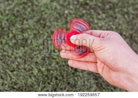 Top view of a hand caucasian man playing with a red fidget spinner on a green lawn background