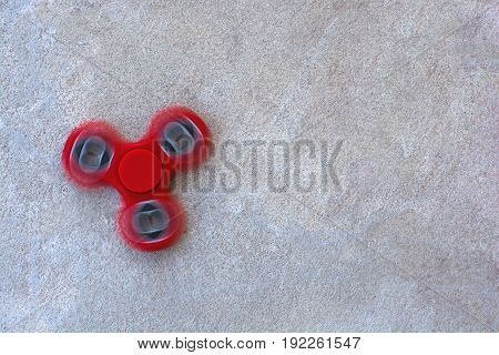 Red fidget spinner in motion stress relieving toy on concrete background.