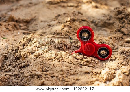Popular red spinner gadget in 2017 against the background of sand. Modern red plastic spinner fidget game for young people.