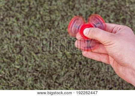 Closeup of a young caucasian man playing with red fidget spinner on f the soccer (football) artificial field. Popular gadget in 2017