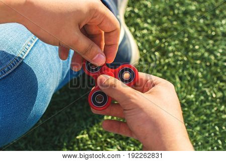 closeup of a young caucasian man playing with a red fidget spinner on nature background. Popular spinner gadget in 2017.