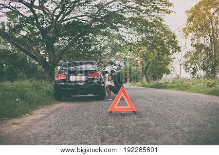 Stressed man sitting after a car breakdown with Red triangle of a car on the road