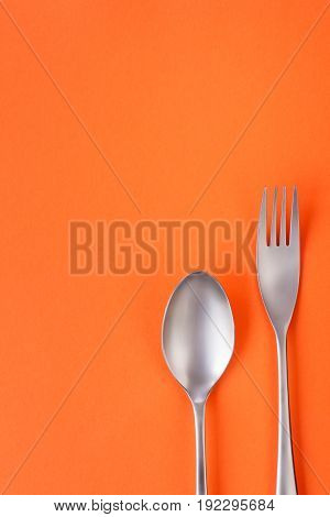 Fork and spoon on orange background sparse composition with copy space. Dinner theme template and background