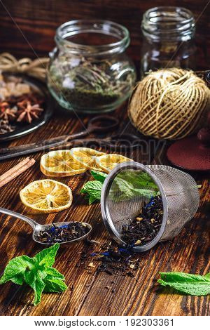 Dry Tea in Spoon and Strainer Fresh Mint and Lemon Slices. Tangle with Two Jars and Teapot on Backdrop.