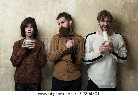 girl standing with cup serious hipster with wine bottle and happy man with milk or yogurt. Group of people or friends with drinks on beige wall. Friendship convive. Healthy or bad habits