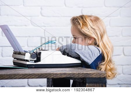 Writer Kid Sitting At Table And Typing Typewriter With Paper