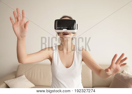 Young woman enjoys VR gaming on sofa at home. Lady excited first virtual reality experience, tries to touch objects in digital simulation app, playing computer games, shopping online with VR technology