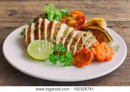 Sliced chicken breast barbecue on white plate served with grilled vegetable. Delicious chicken breast steak and salad for dinner. Homemade chicken breast barbecue on wood table for background. Chicken barbecue or pork steak.