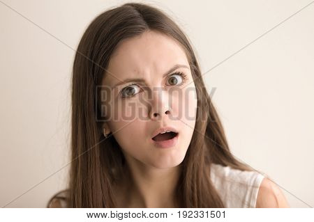 Headshot portrait of confused young woman. Beautiful teen girl with shocked facial expression looking at camera with surprise. Lovely lady feeling resentment, misunderstanding. Close up. Front view