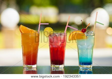 Three glasses of non-alcoholic drink and fruit on a table with a blurred background.