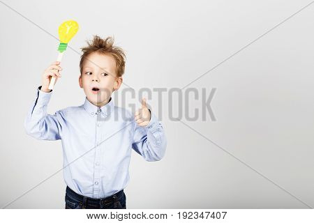 Cute Little School Boy With Yellow Paper Lightbulb Against A White Background. Cheerful Smiling Kid