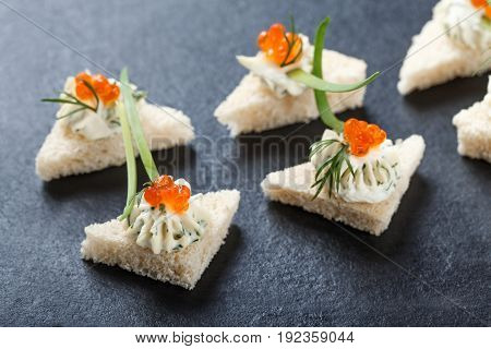 Appetizer canape with red caviar and cream cheese on stone slate background close up. Delicious snacks sandwiches crostini brushetta antipasti on party or picnic time. Top view