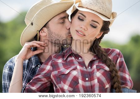 young cowboy kissing his sensual girlfriend outdoors at daytime