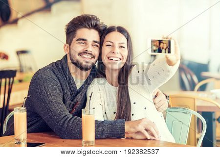 Beautiful young couple making selfie using a smartphone and smiling while sitting in the cafe.