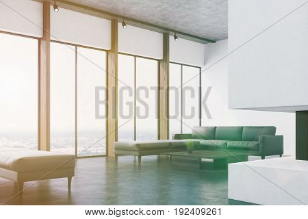 Corner of a white living room interio with a concrete floor panoramic windows a fireplace a long gray sofa and a narrow coffee table. 3d rendering mock up toned image