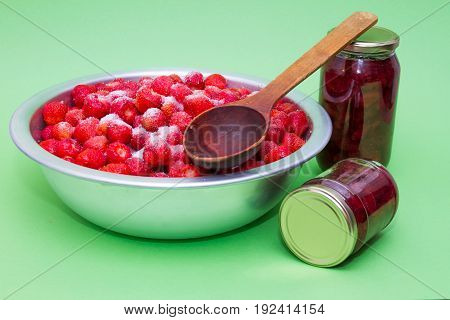 Strawberries from the manufacturer with sugar and jars for making jam on a green background.