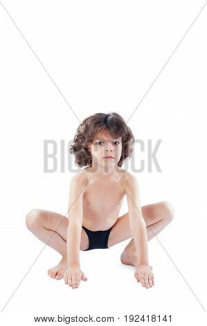 The curly-haired boy in a bathing suit sits in a pose of a frog looking at the camera. Blue background.