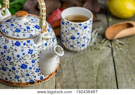 Glass of tea with tea pot and lemon on natural wooden table.