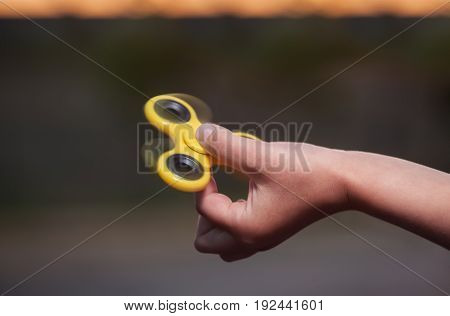 Little Girl Is Playing A Yellow Spinner In Her Hand Outdoors.