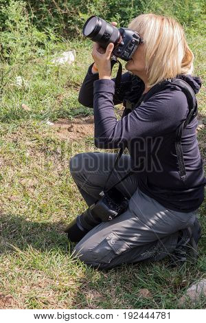 Nilgiri Hills India - October 26 2013: Kneeled blonde photographer takes picture in Masamigulli Forest. She holds two heavy DLRS cameras. Face hidden.