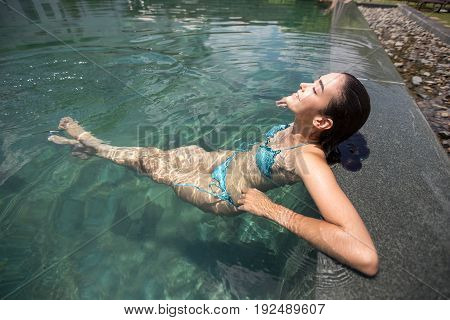 Portrait of young Caucasian woman wearing bikini having pleasure sitting in outdoor spa or hotel swimming pool