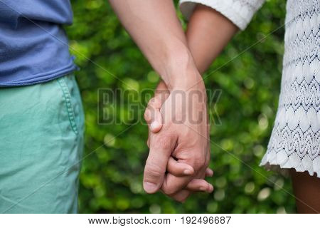 Cropped view of couple holding hands with green leaves wall in background. Front view.