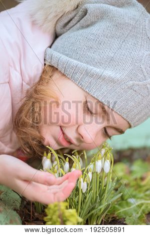 Little girl touching flowers snowdrops growing in the flowerbed