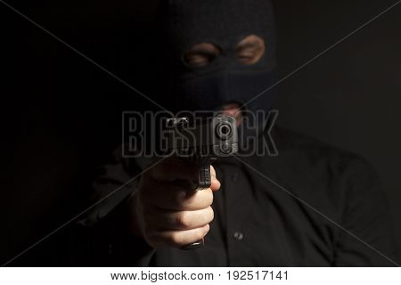 criminal bandit man wearing in balaclava holds a gun in his hand on black background